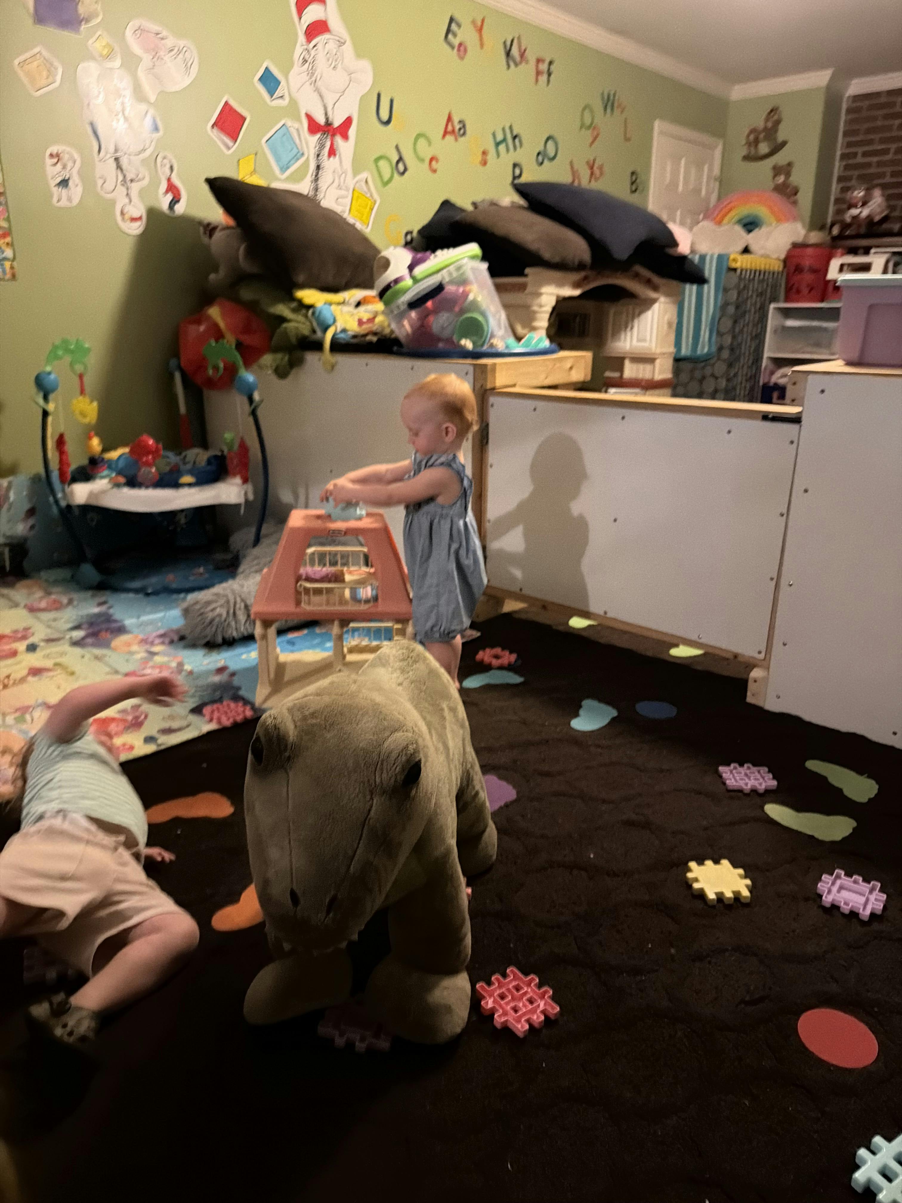 Two children playing in a playroom with a large plush dinosaur and floor toys