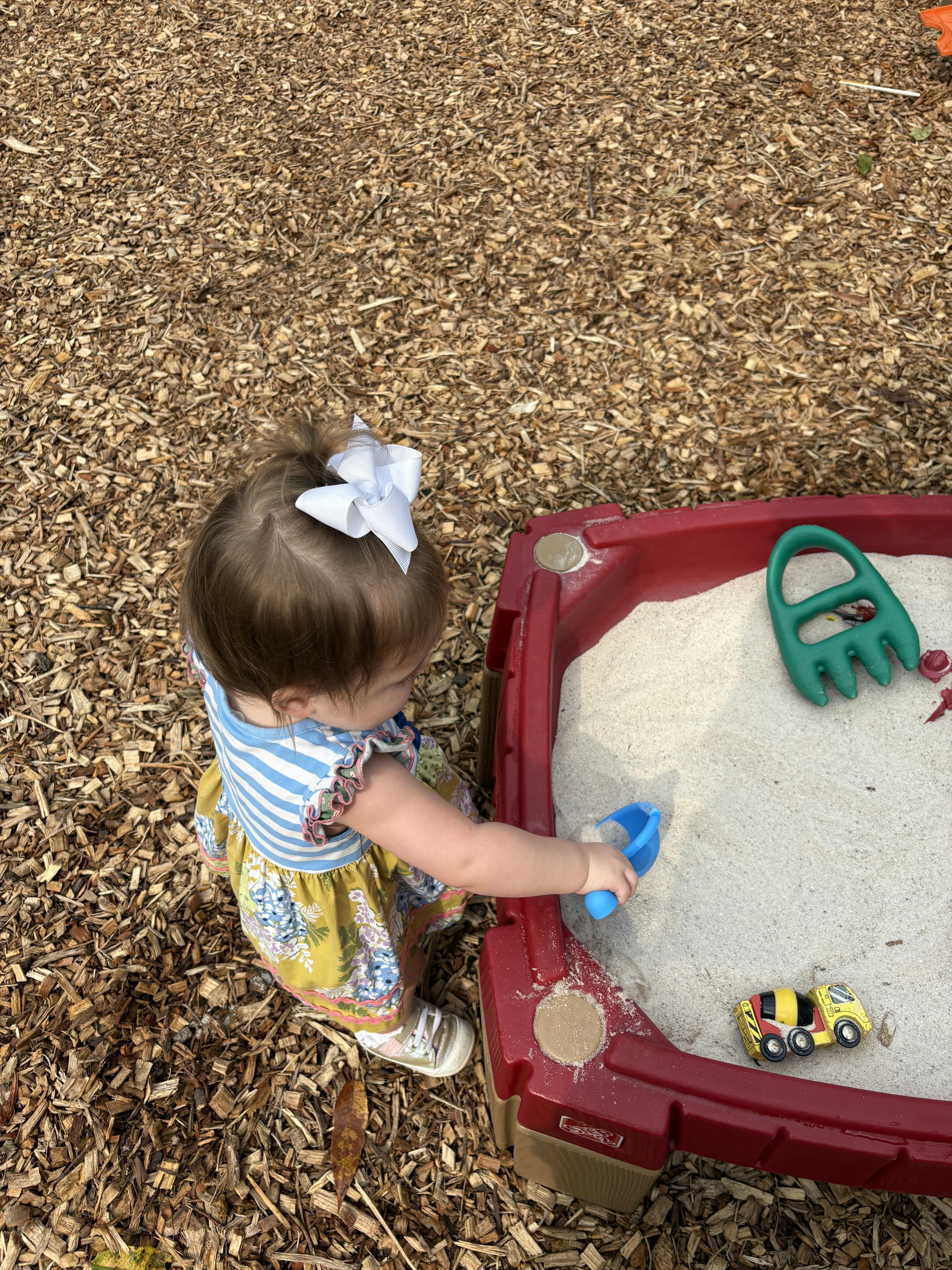 Child playing in a sandbox with a blue shovel