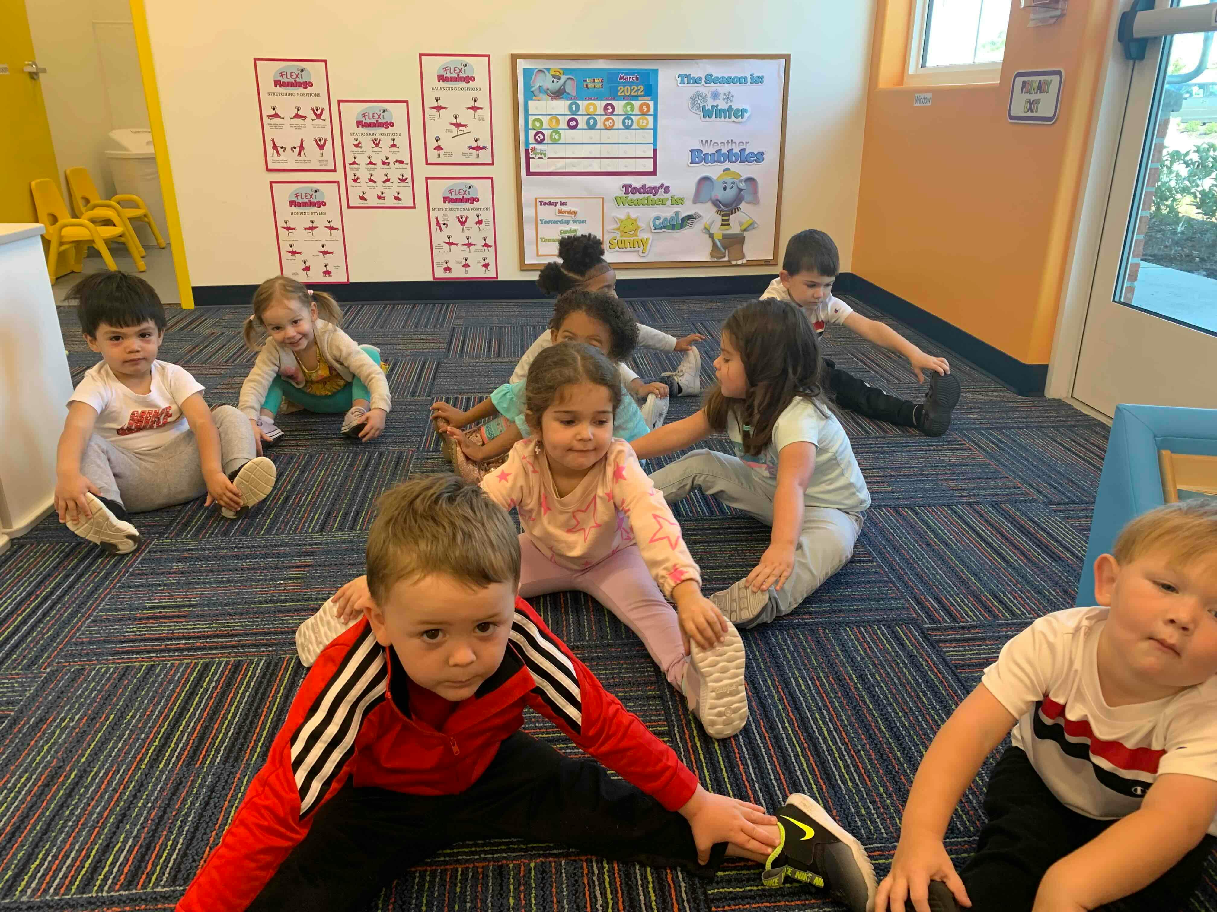Children sitting on a carpeted floor, stretching their legs