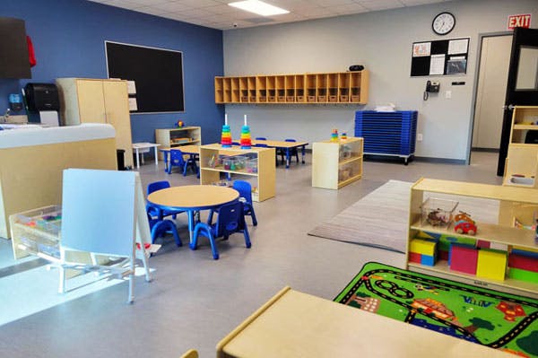 Empty classroom with small tables and chairs, cubbies, and play areas