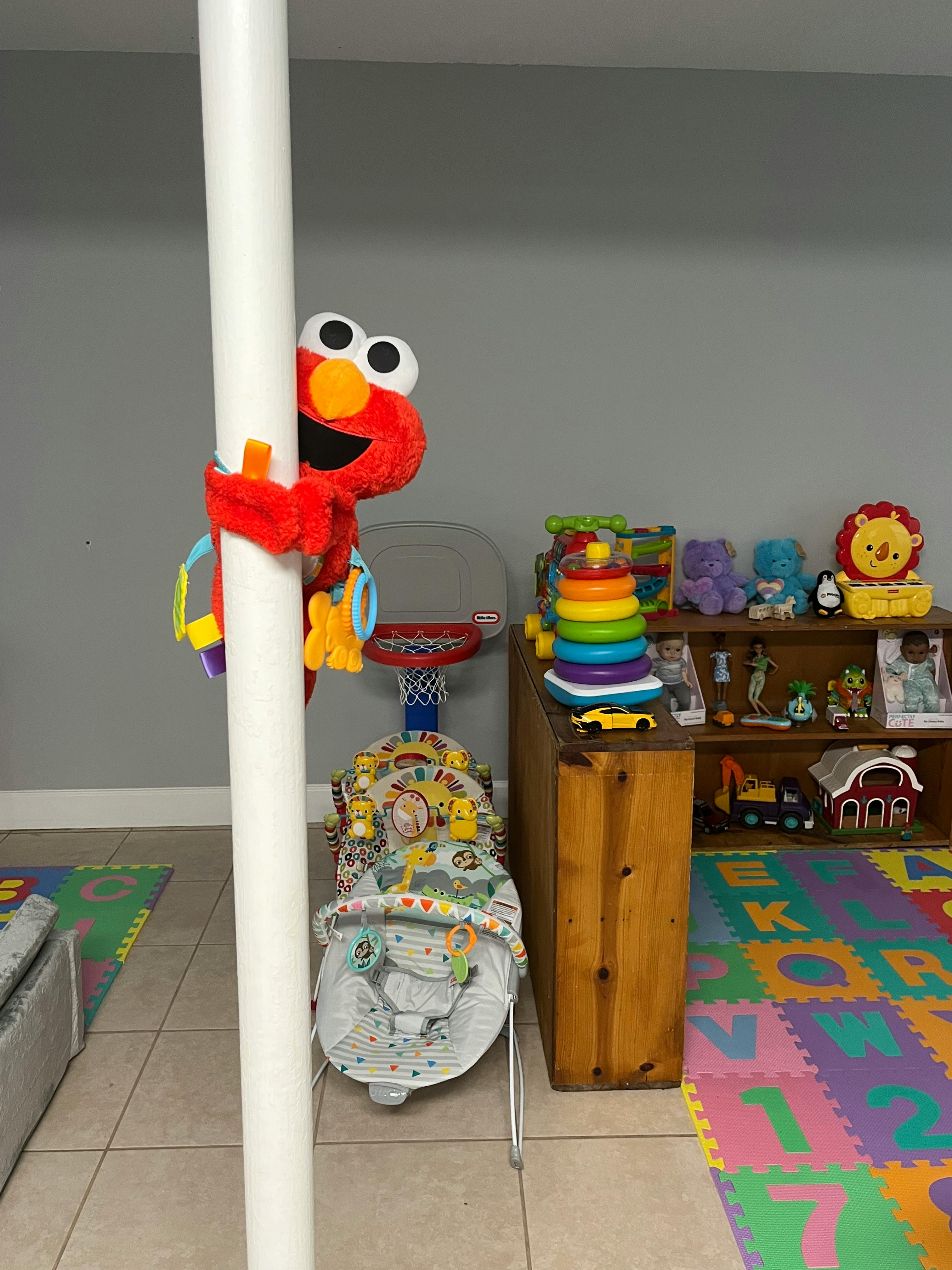 Elmo plush toy on a pole in a room with children's toys