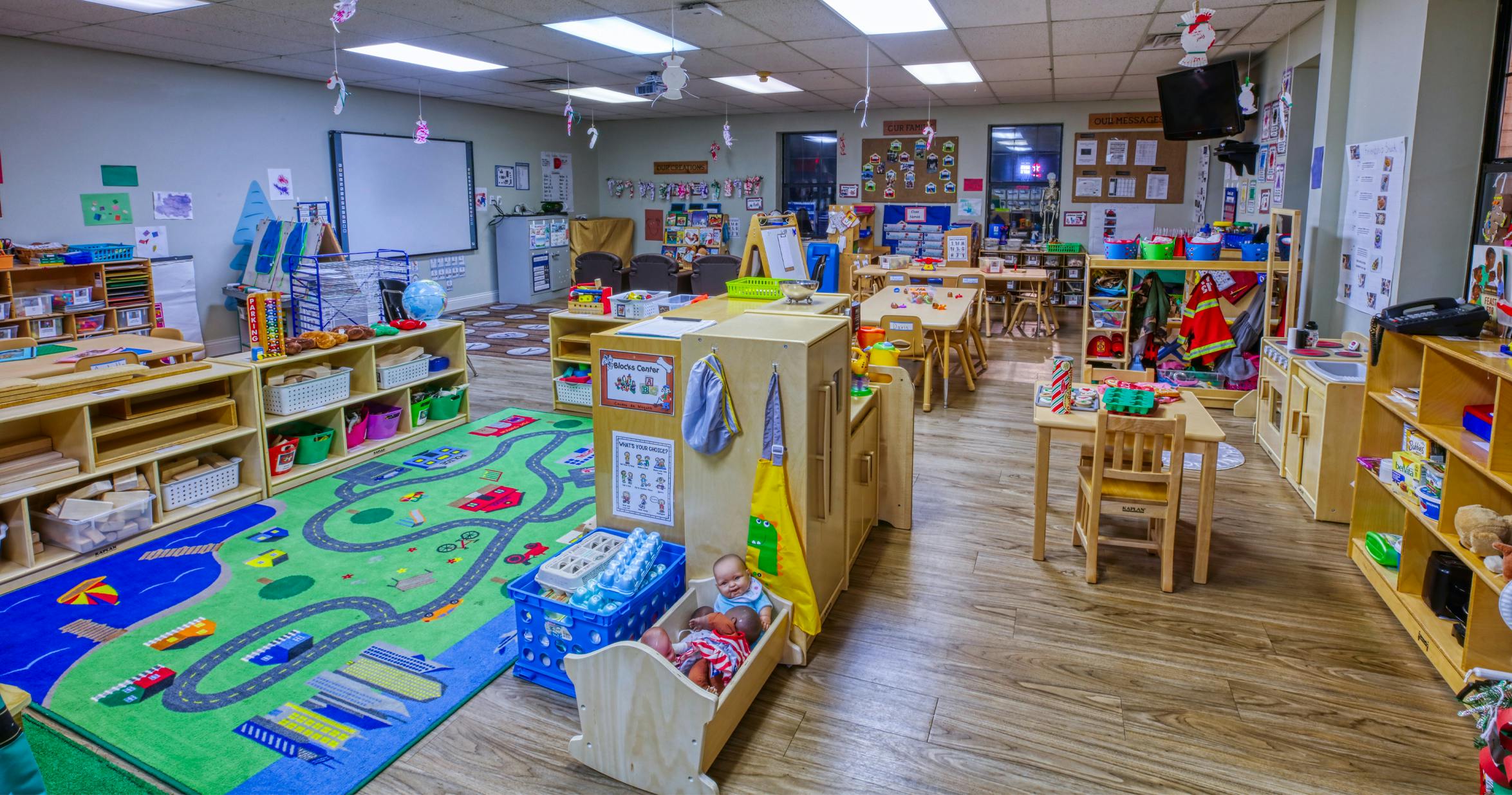 A classroom with activity areas, child-sized tables, shelves, and a play rug