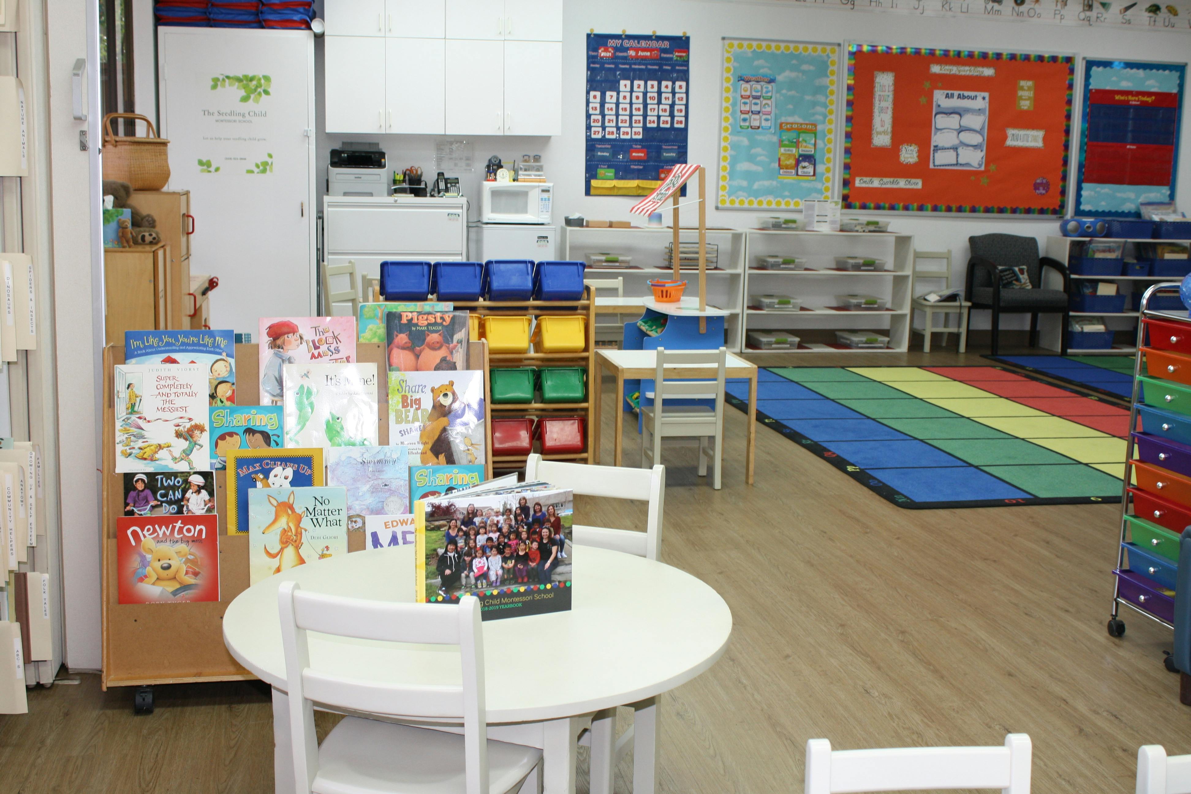 Classroom with tables, chairs, bookshelves, and colorful mats