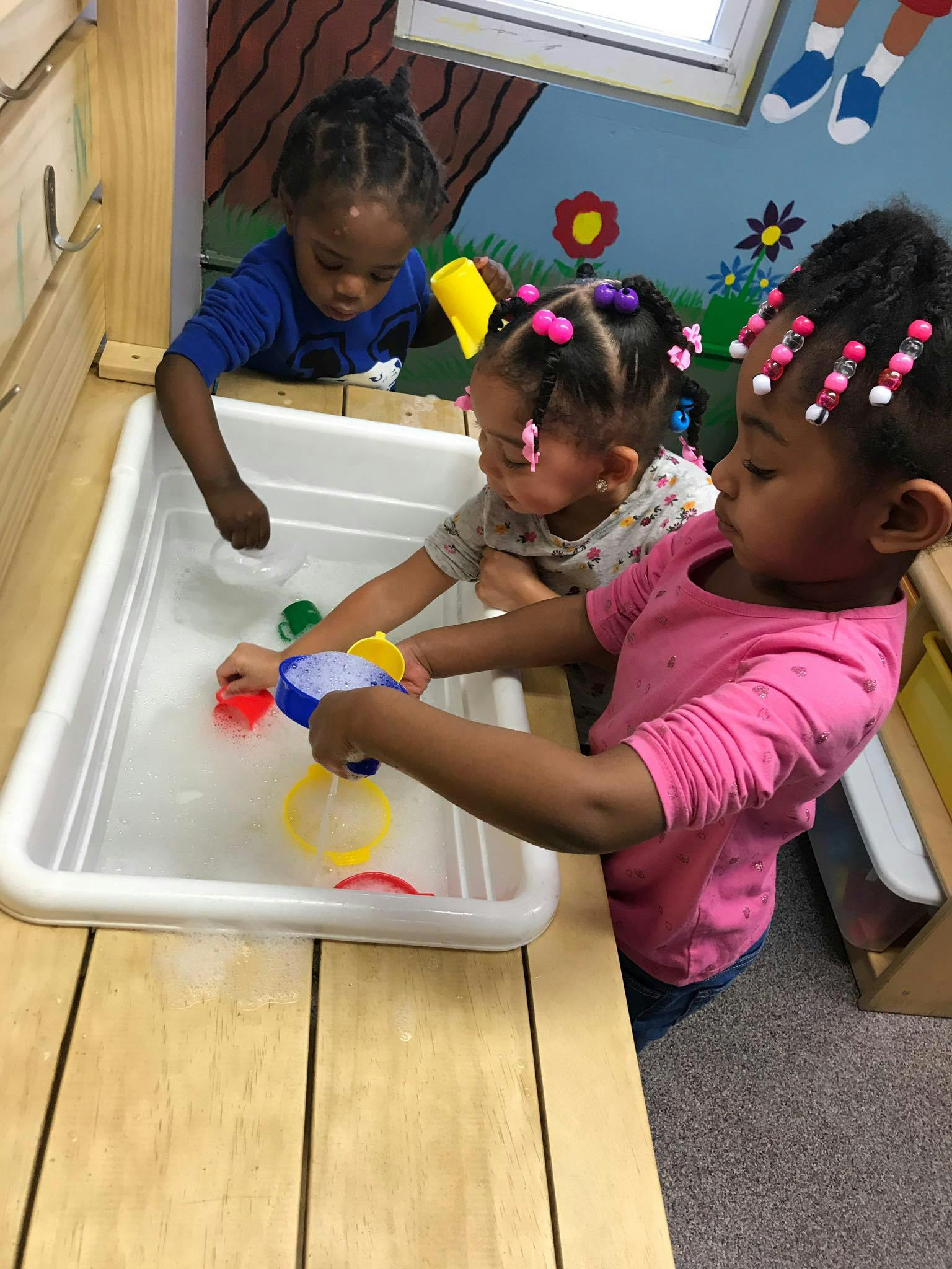 Three children playing with water and toys in a sensory bin