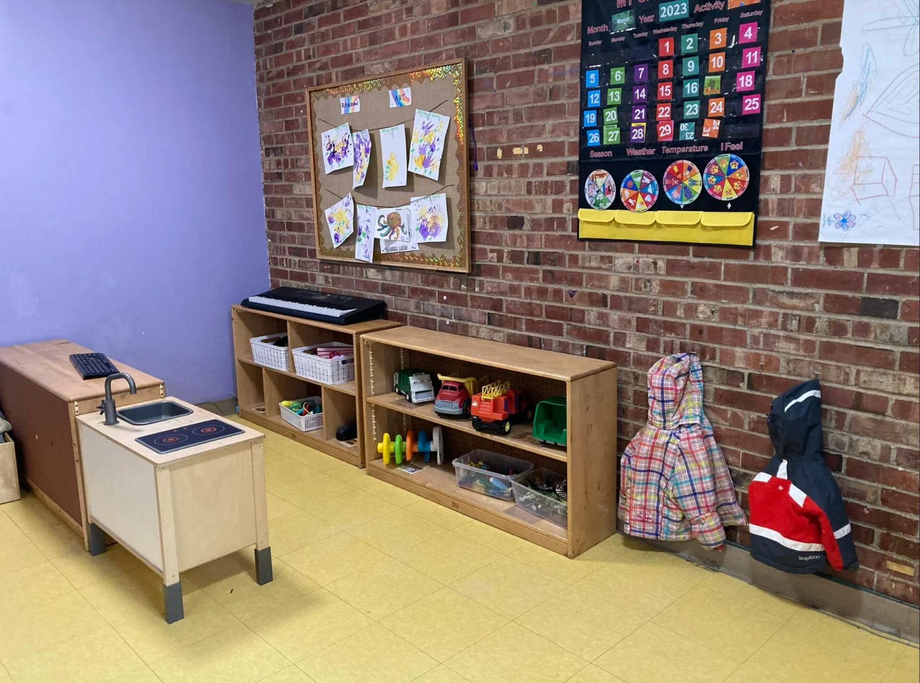 Classroom interior with toy kitchen shelves artwork and a calendar