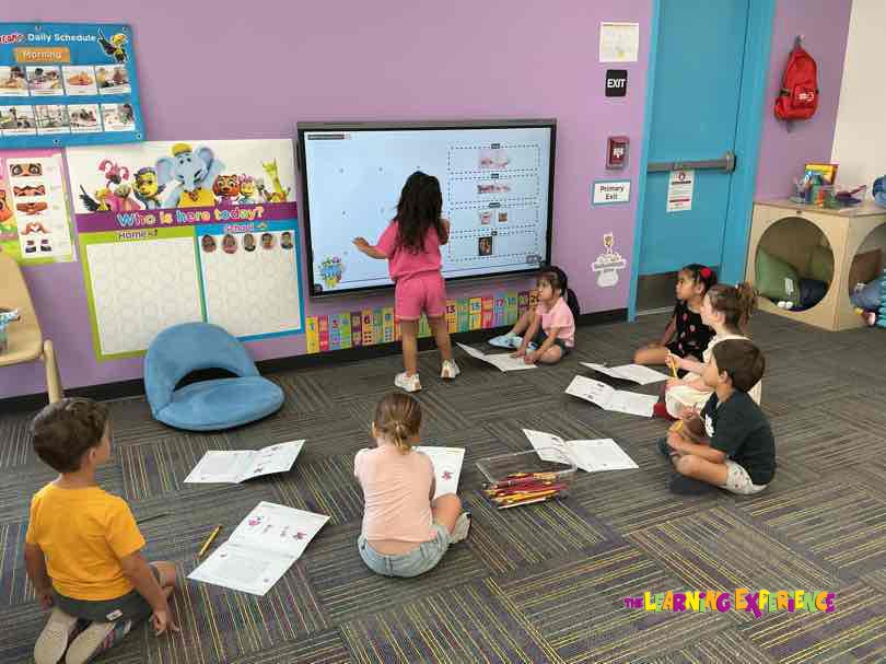 Child standing in front of a large screen with other children sitting on the floor