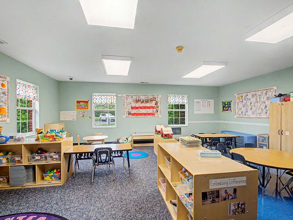 Classroom with tables, chairs, shelving units with toys, and windows