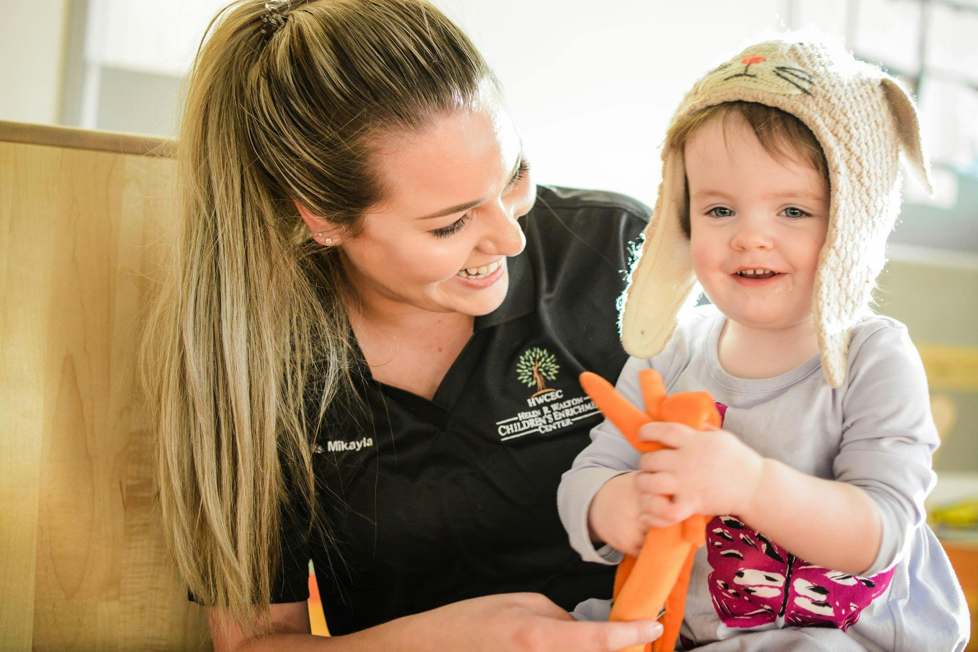 Person smiling at a child in a hat holding an orange toy