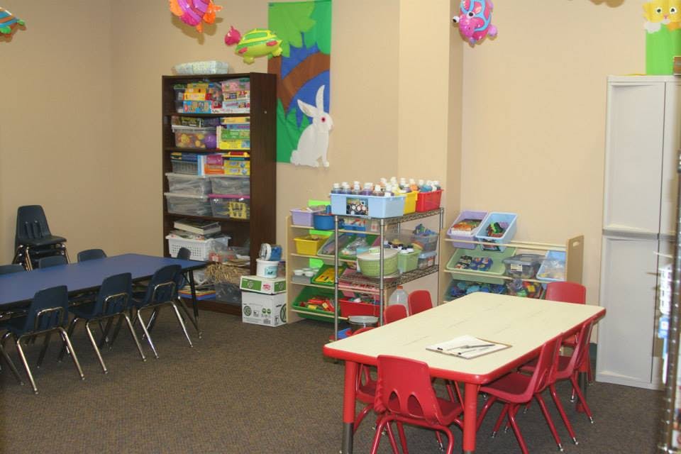 Classroom with small tables and chairs, shelves with toys and supplies