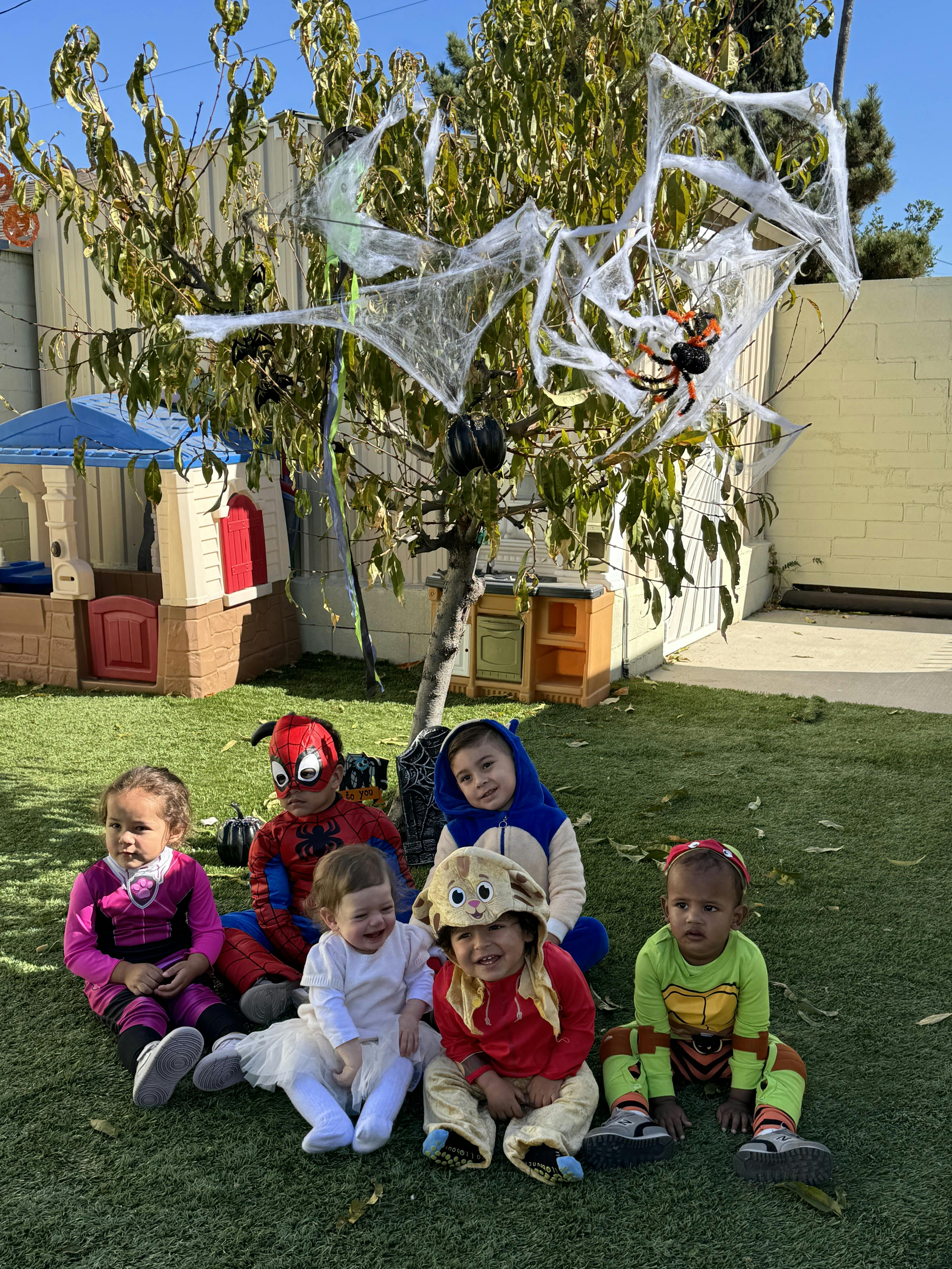 Children in costumes sitting on grass with Halloween decorations