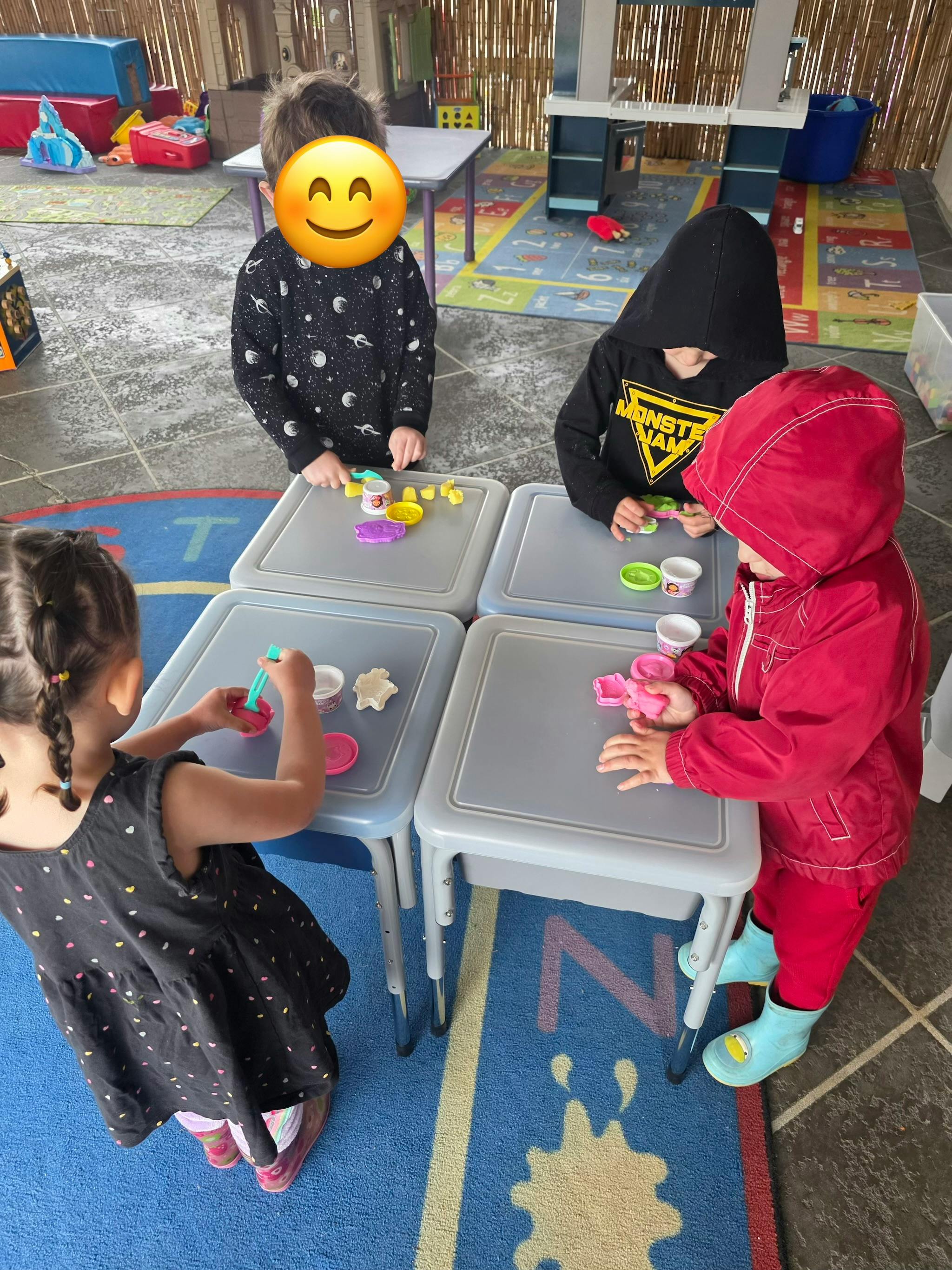 Four children playing with modeling clay at small tables in a classroom