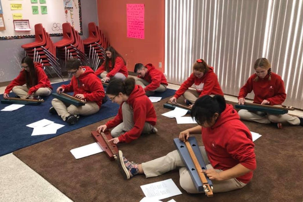 Children in red shirts playing stringed instruments on the floor