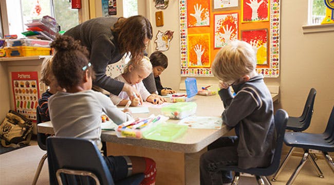 Adult helping children at a table in a classroom