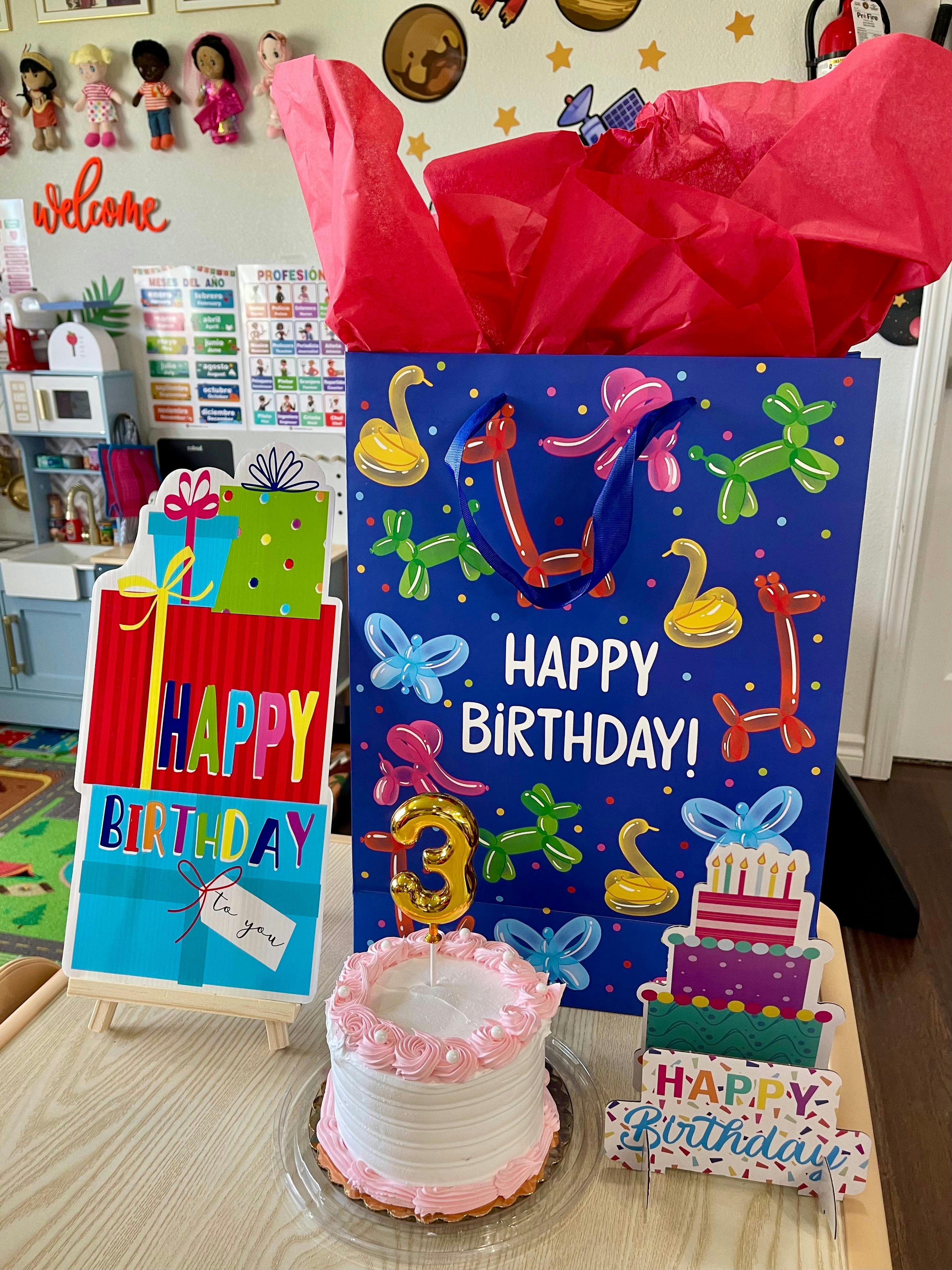 Birthday cake with a number three candle in front of birthday gift bags