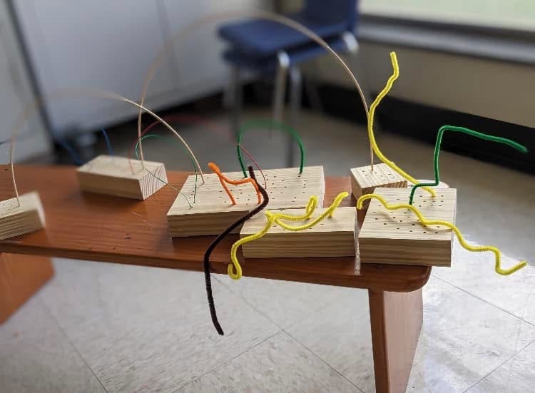 Pipe cleaners inserted into holes in wooden blocks on a table