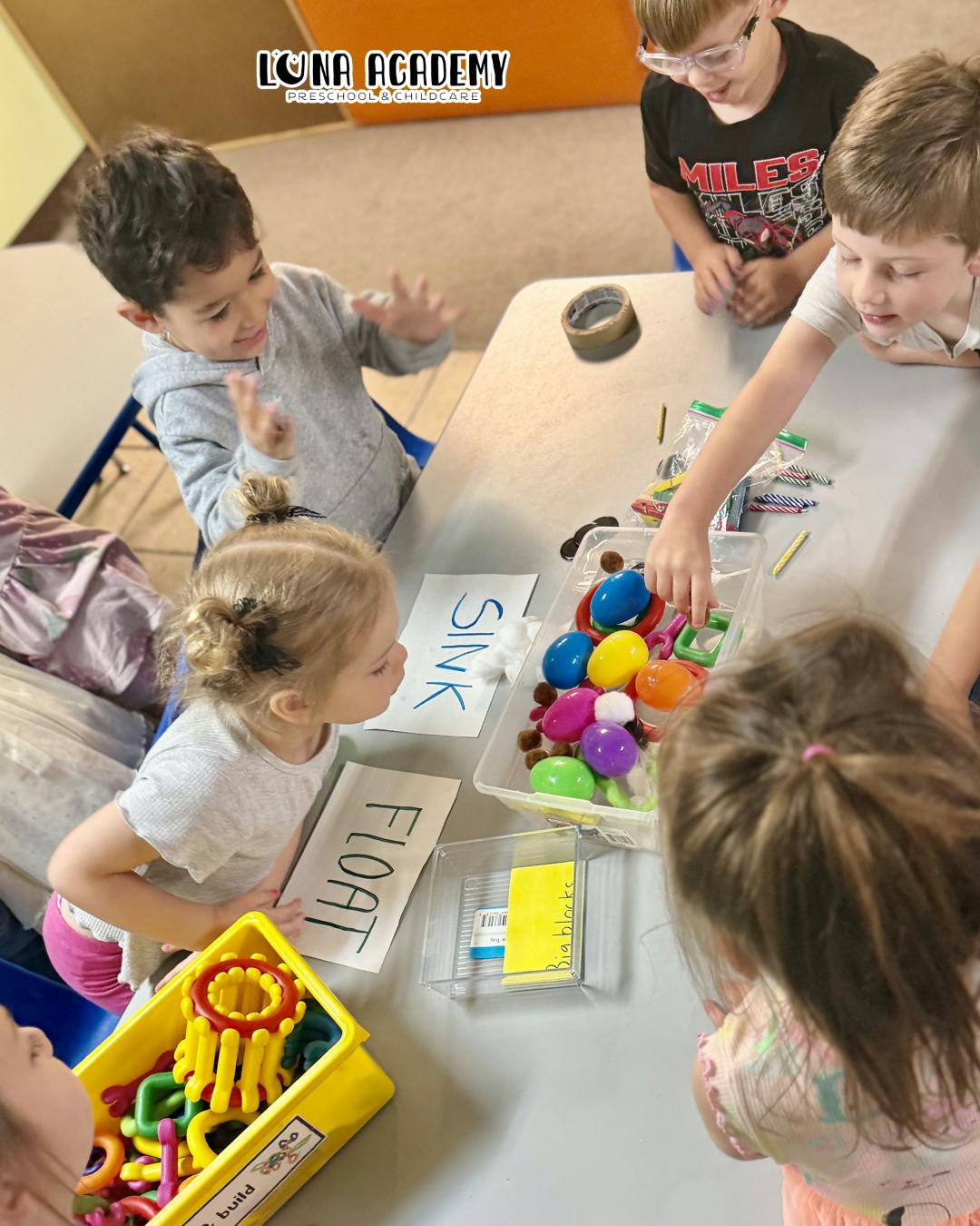 Children gathering around a table for a science activity with sink or float labels