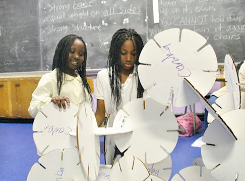 Two teens building a structure with white cardboard pieces in a classroom