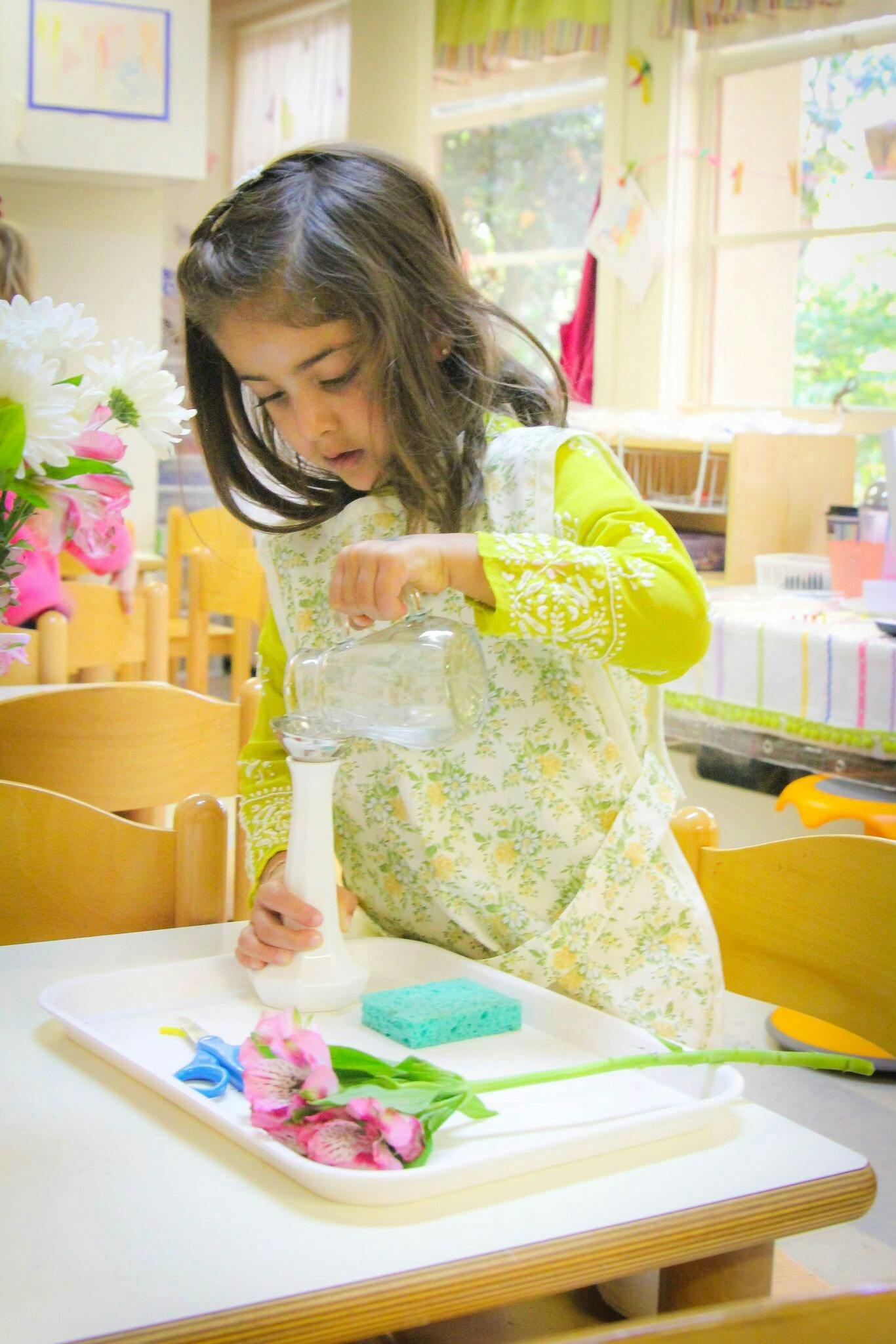 Child pouring water into a vase with flowers on a tray