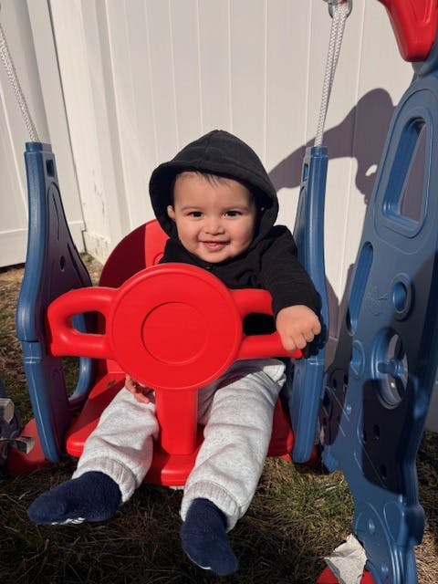 Child with black hooded shirt sitting in a red and blue swing