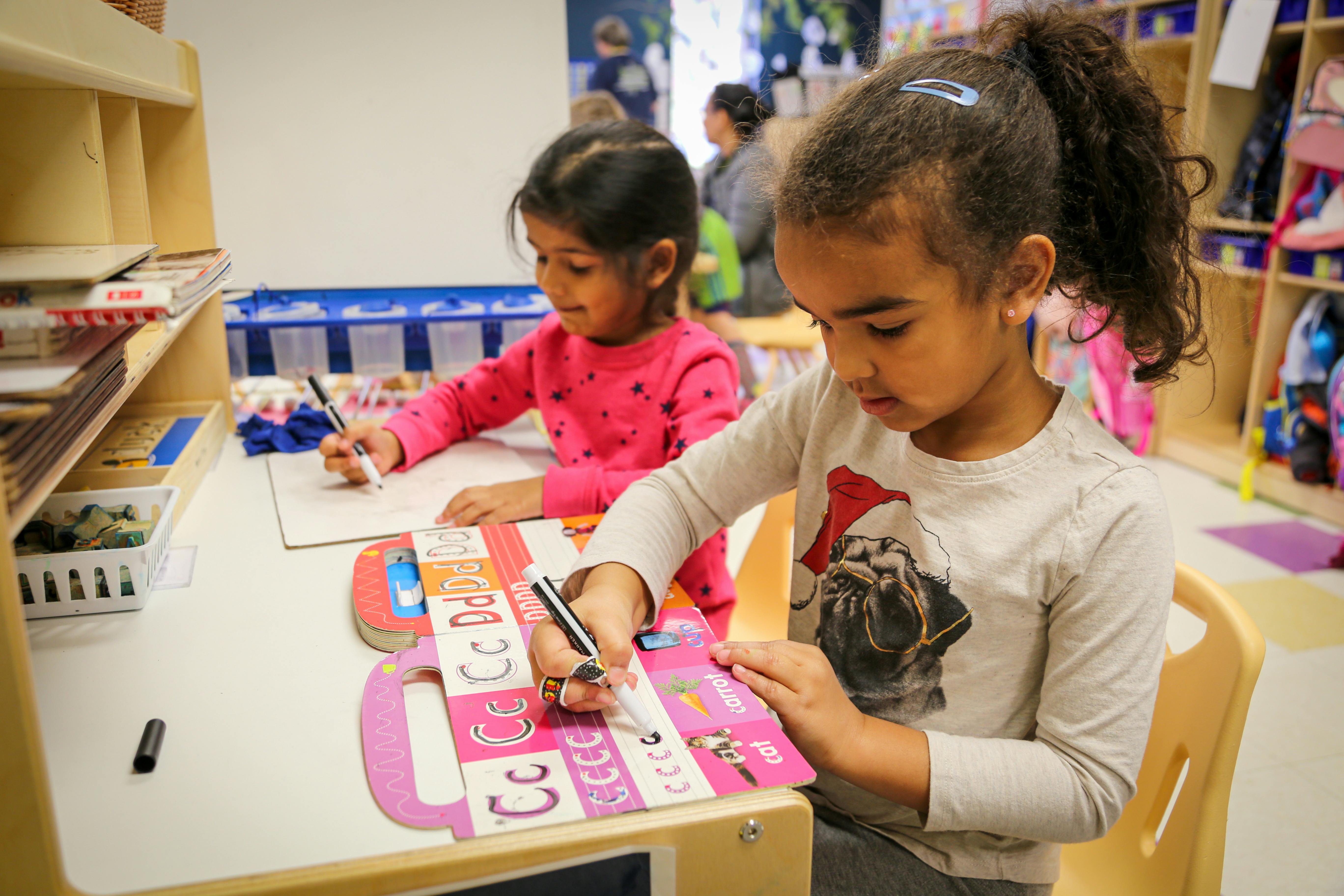 Two children writing at a table in a classroom
