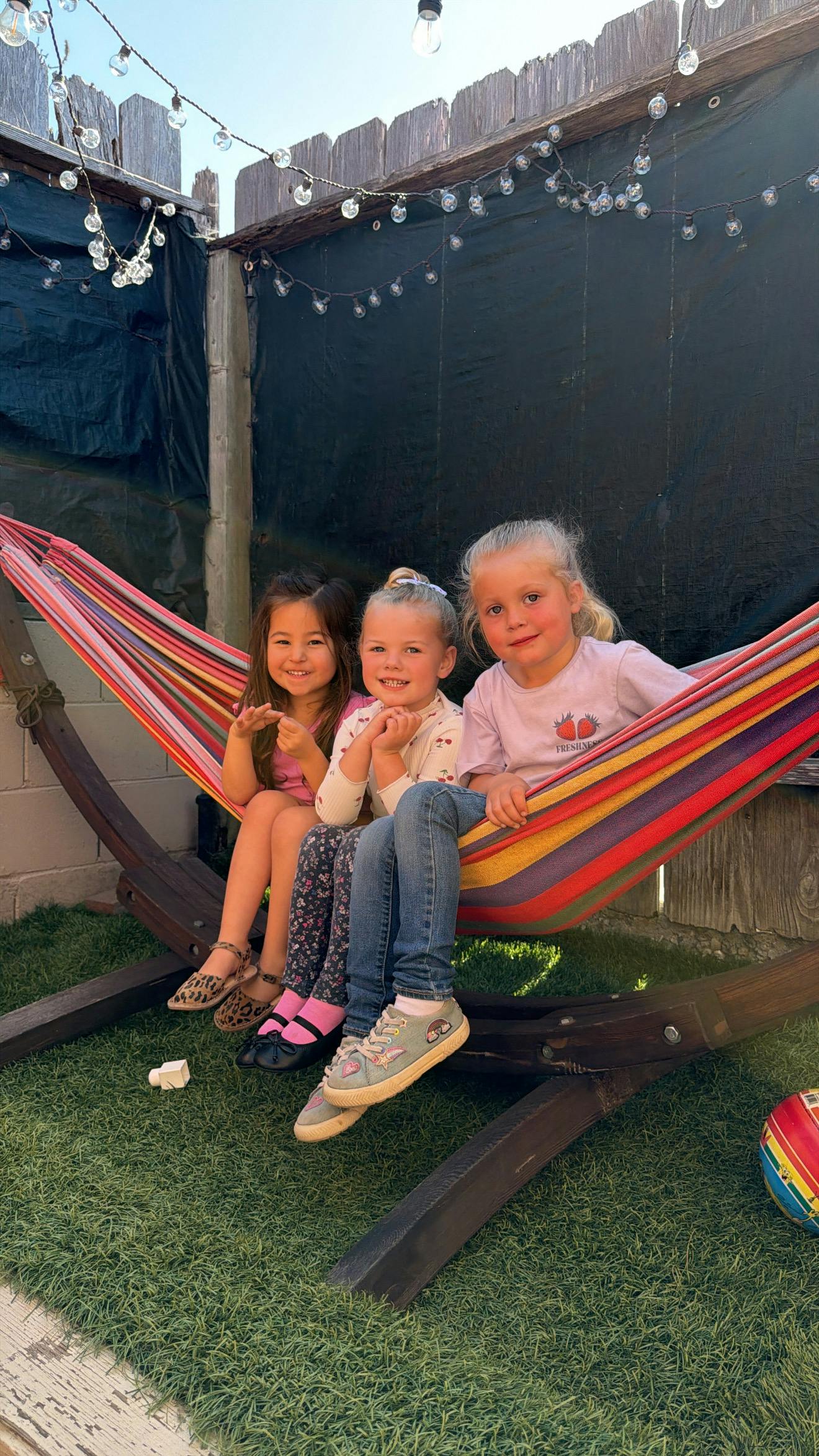 Three children sitting in a colorful striped hammock