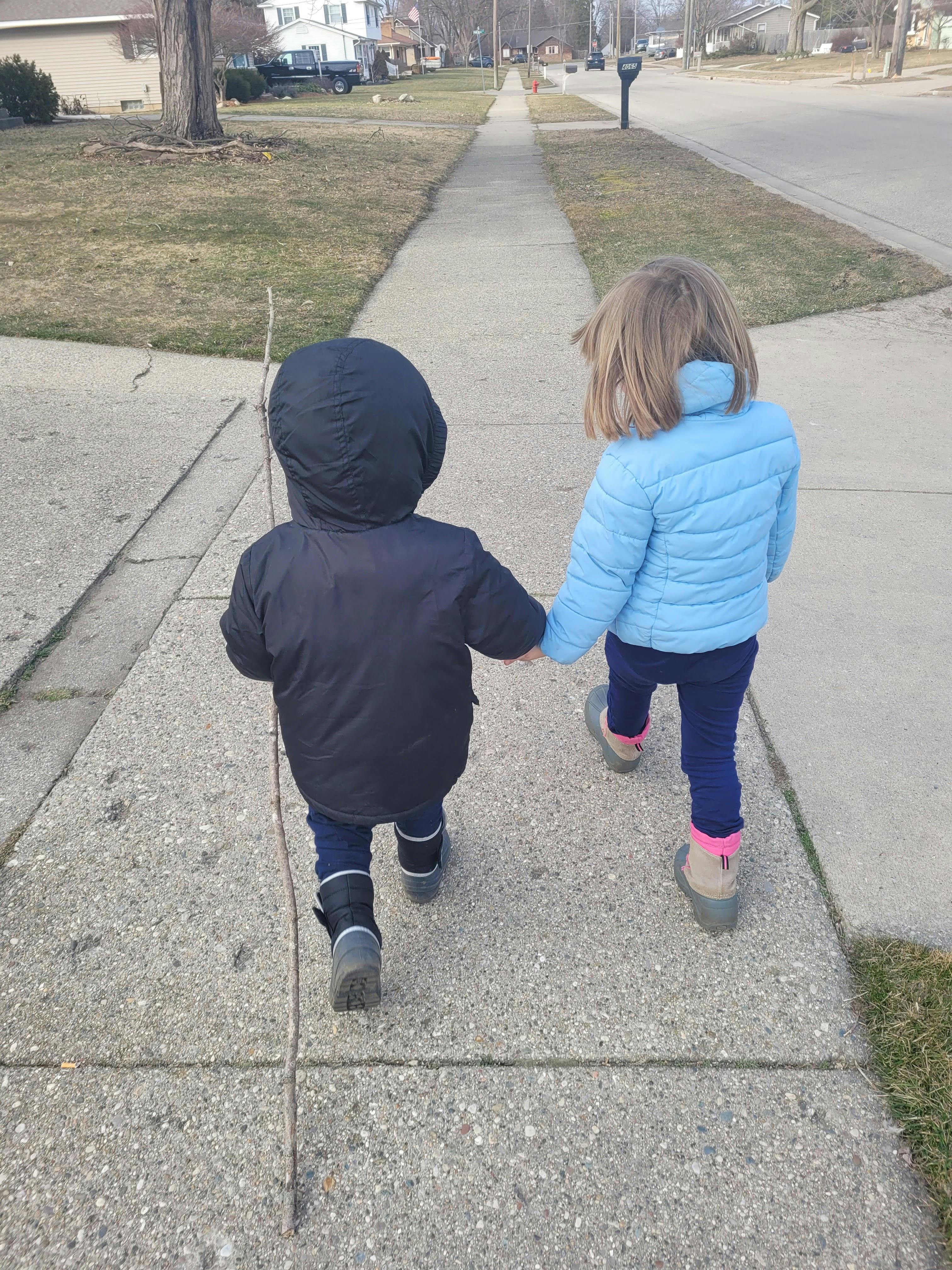 Two children walking on a sidewalk holding hands