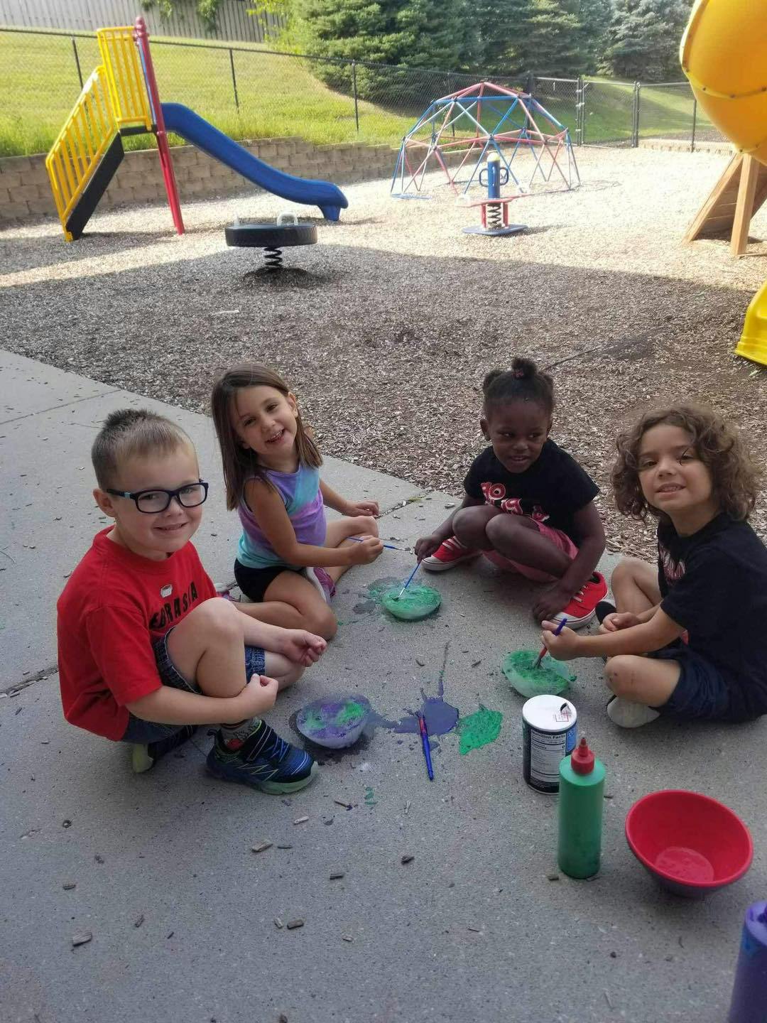 Four children sitting on the ground painting