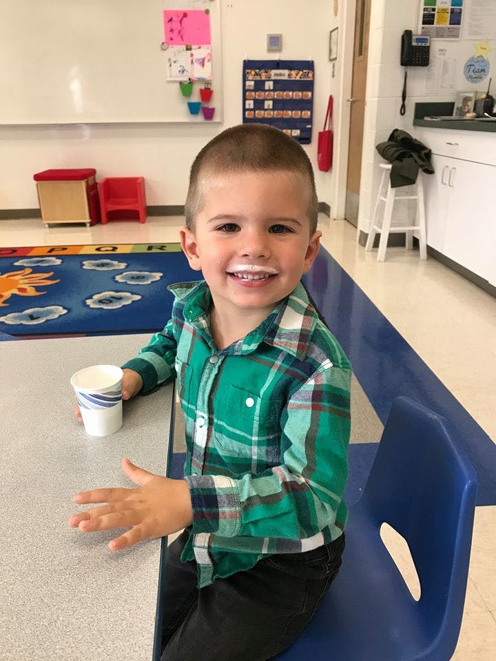 Child with milk mustache holding a cup at a table