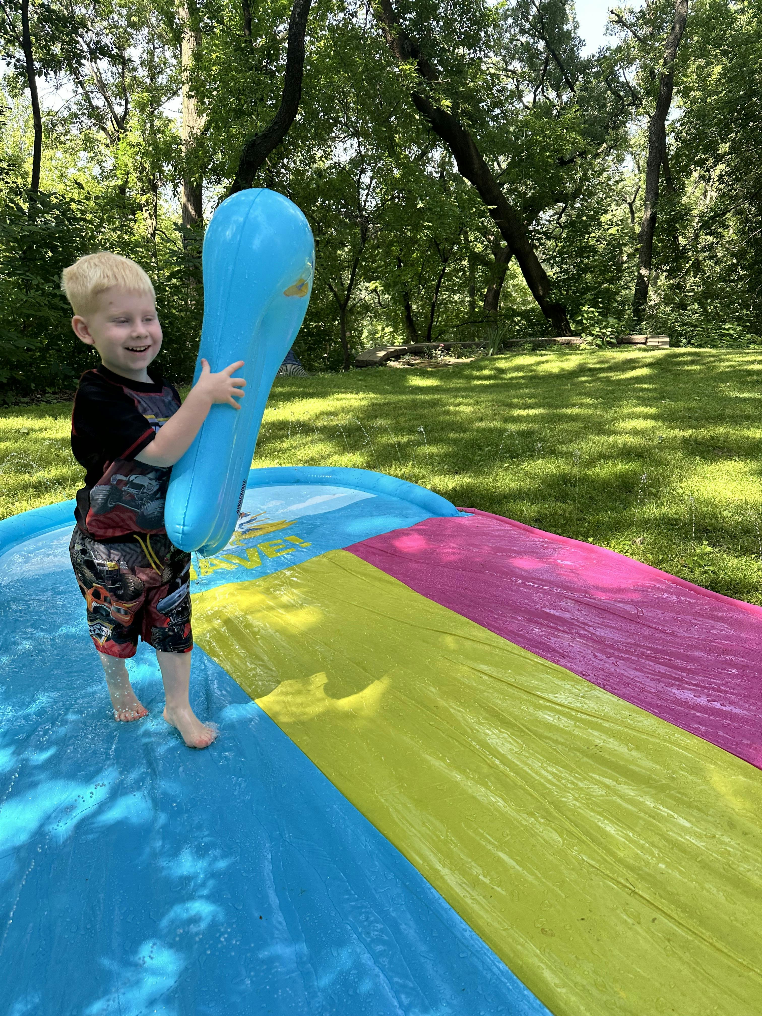 Child on a multicolor water slide holding a blue inflatable toy