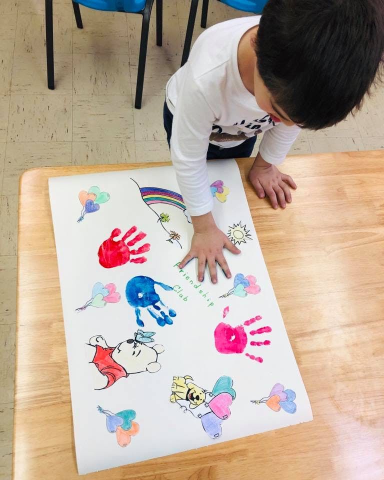 Child looking at a paper with colorful handprints and drawings