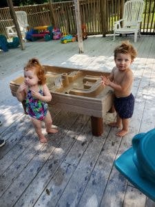 Two children playing with a water table on a deck