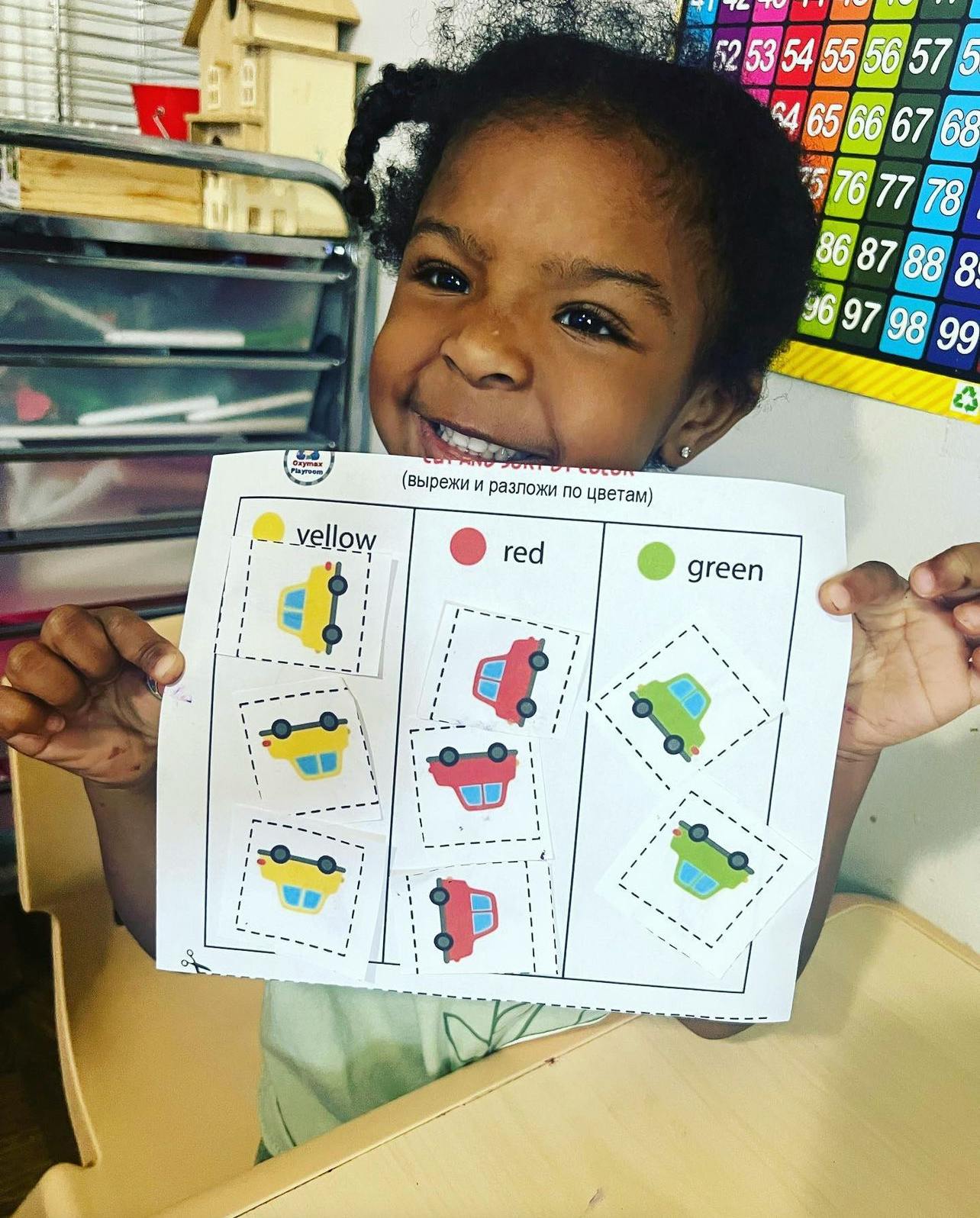 Child holding up a paper with yellow, red, and green car cutouts
