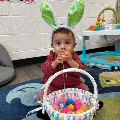 Child wearing bunny ears and holding an Easter egg, with a basket of eggs