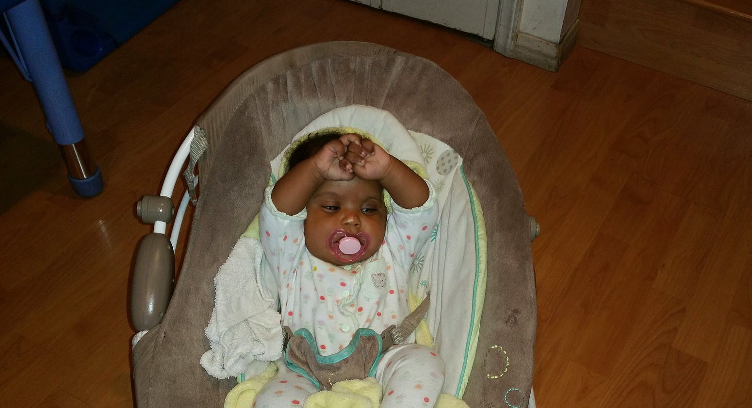 Child in a baby bouncer with hands near head and pacifier in mouth