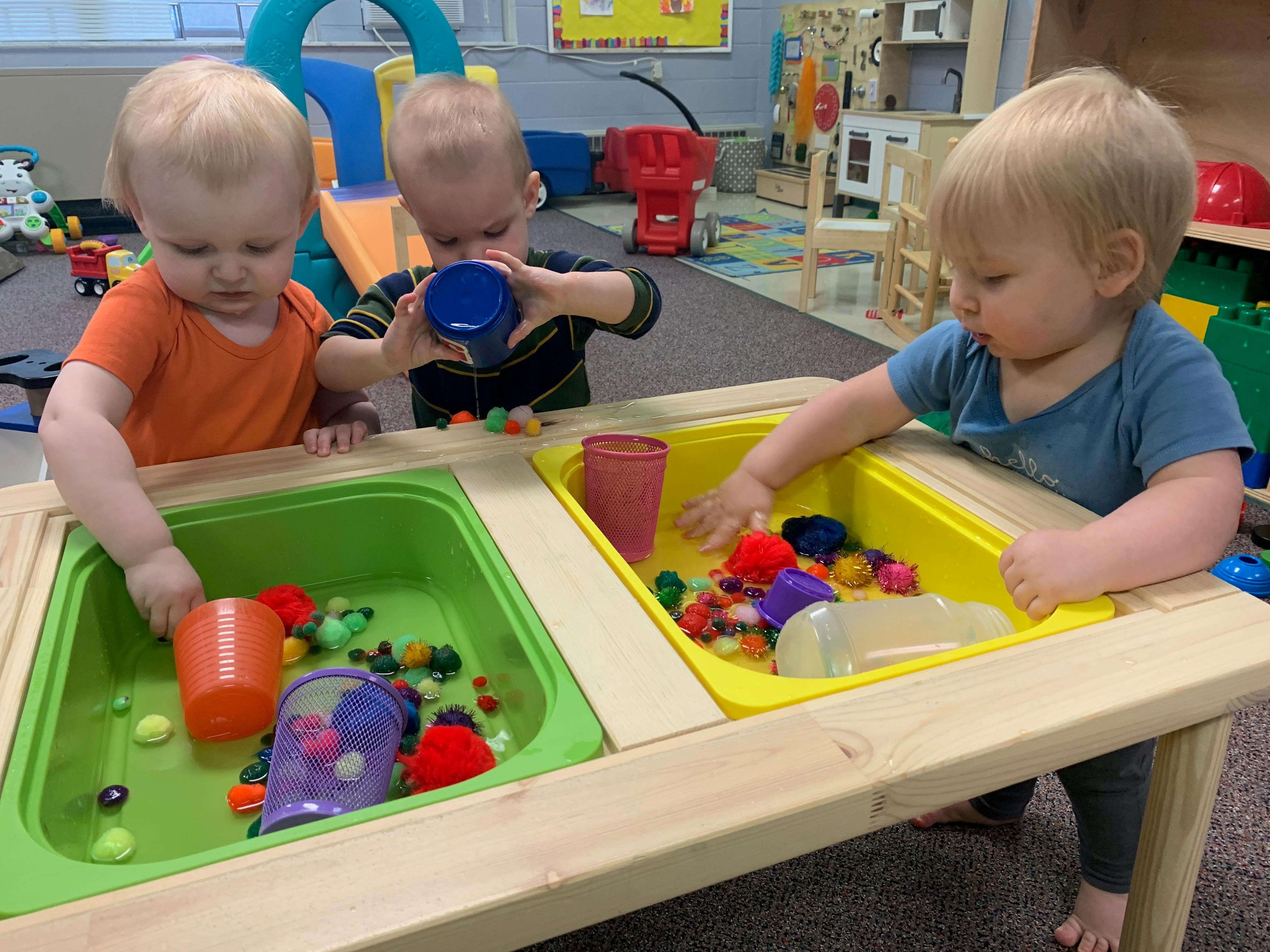 Three children playing with colorful objects in sensory bins