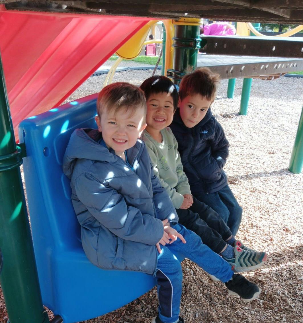 Three children sitting on a blue structure on a playground