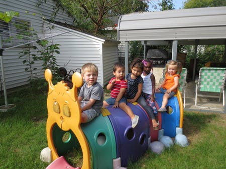 Five children sitting on a colorful caterpillar playground toy outdoors
