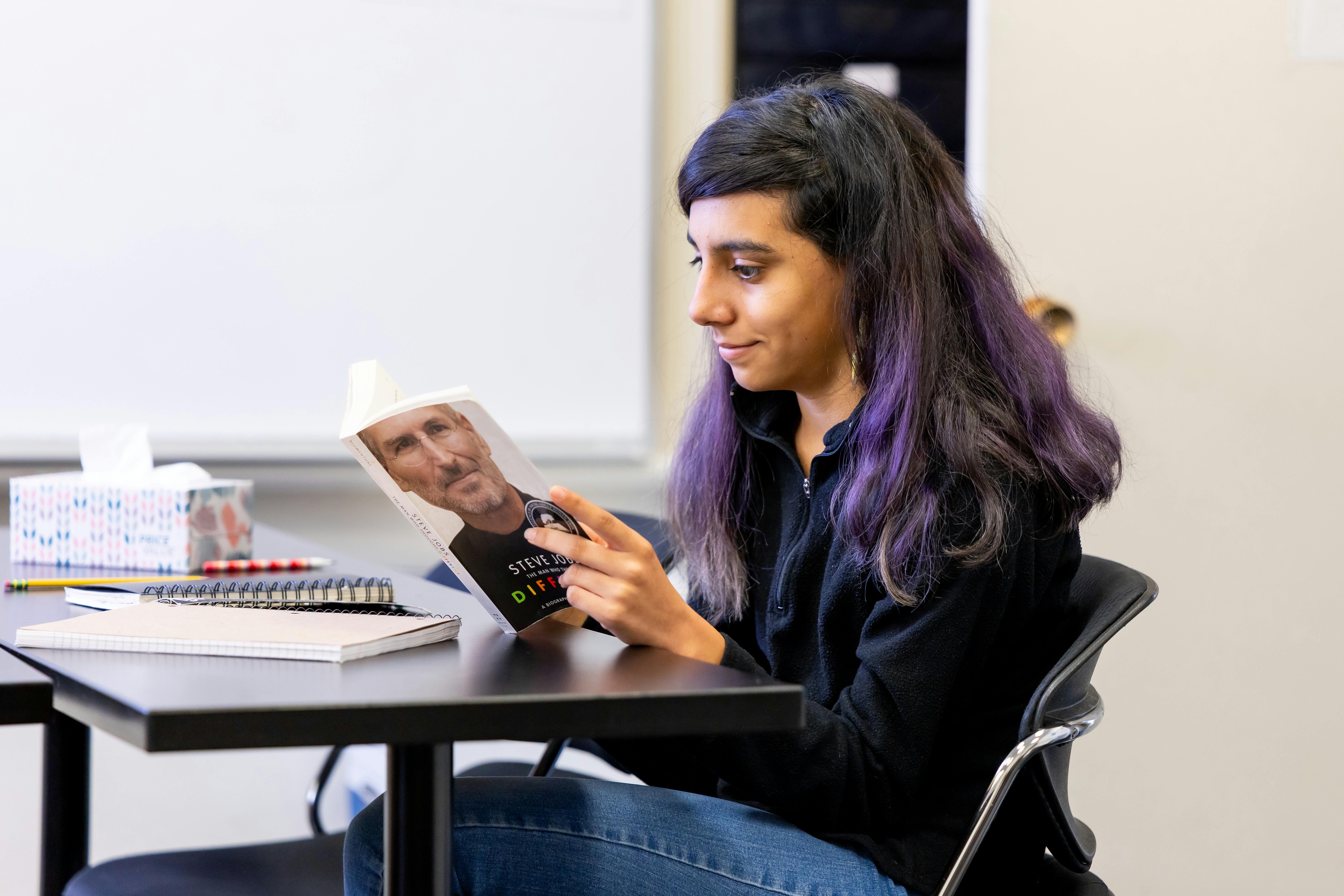 Person with purple-streaked hair reading a book with "STEVE JOBS" on the cover