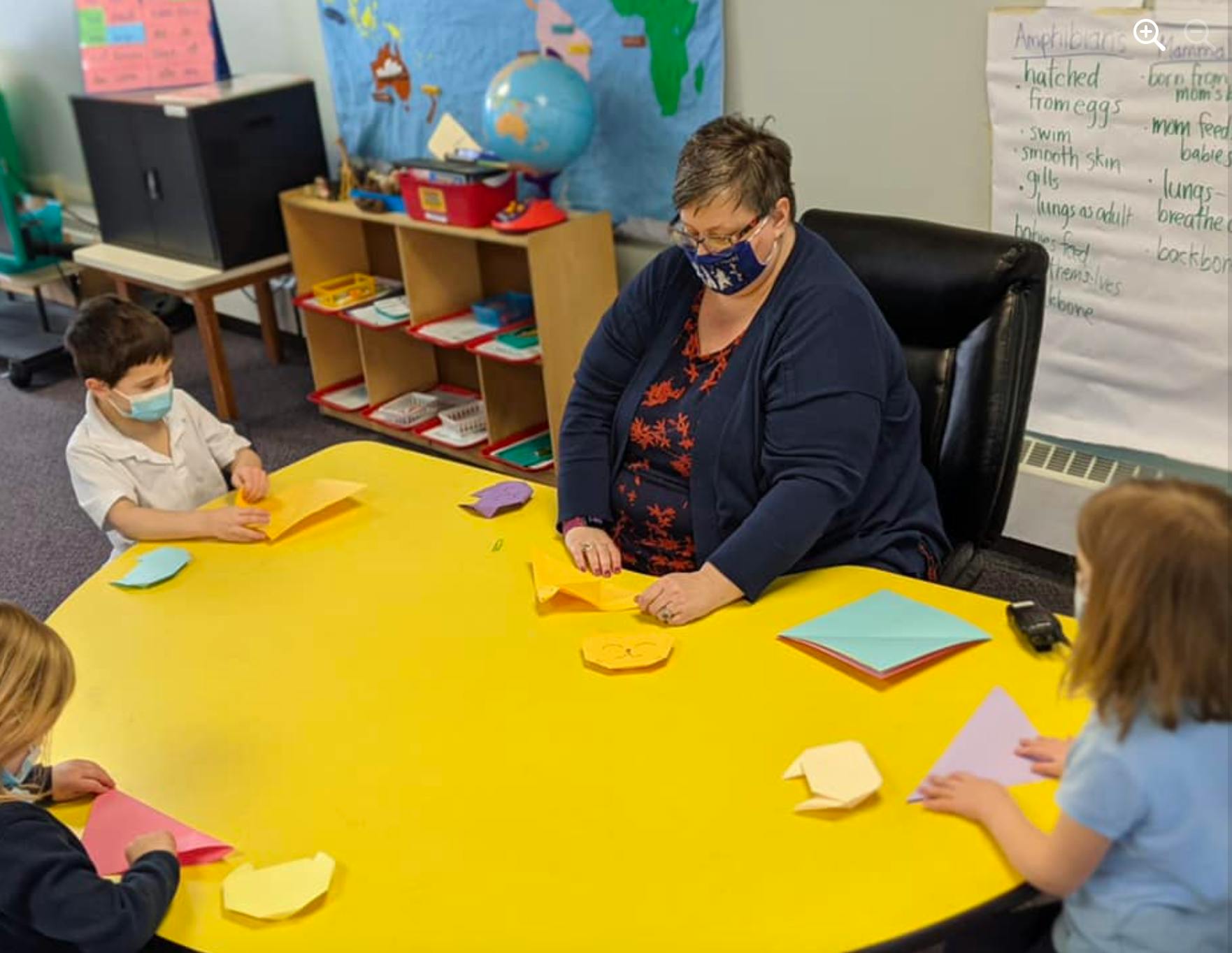 Adult and two children at a yellow table with paper crafts