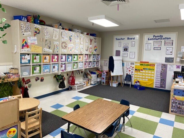 An empty early childhood classroom with cubbies, tables, chairs, and learning charts