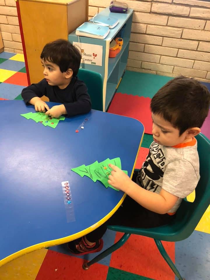 Two children at a table with green paper cutouts