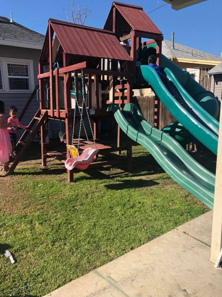 Children playing on a wooden playset with green slides and a swing