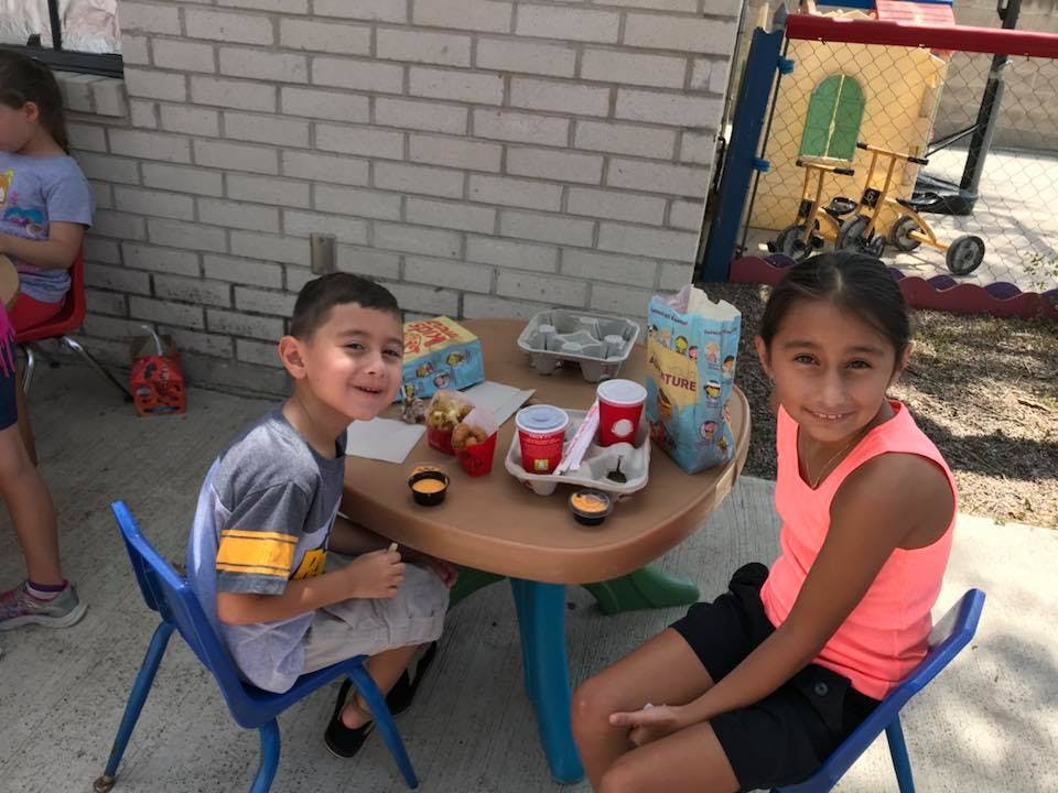 Two children sitting at a small table with snacks and drinks