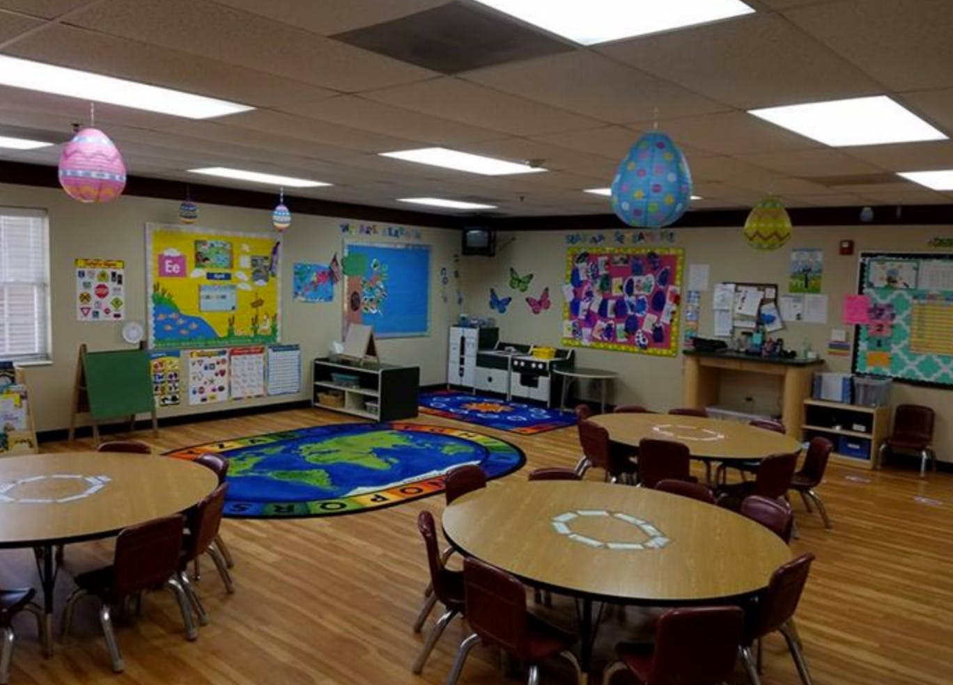 Empty classroom with small tables and chairs, colorful rugs, and decorations