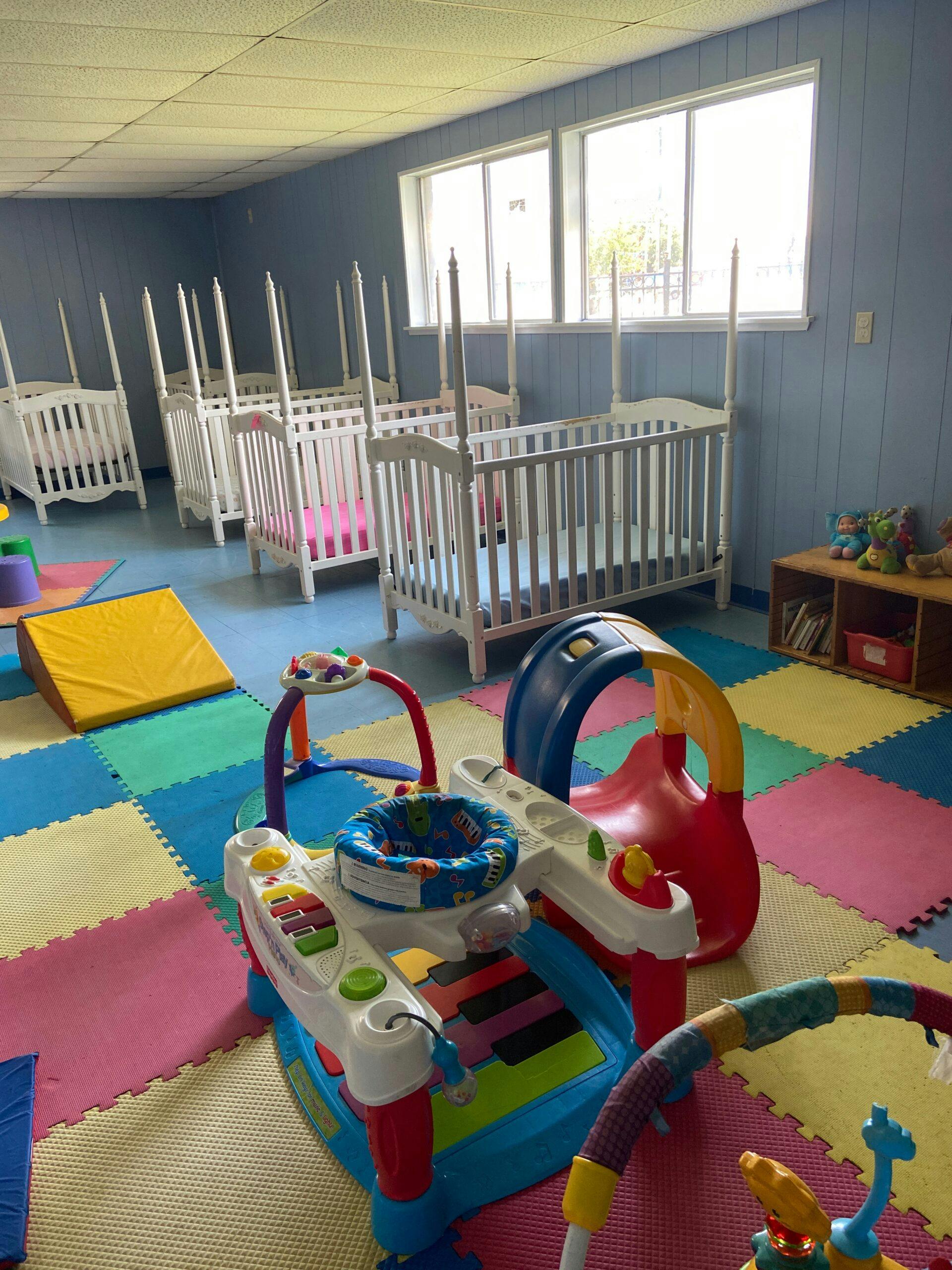 Nursery room with multiple white cribs and colorful play mats