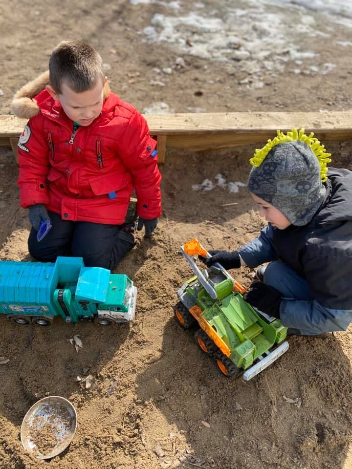 Two children playing with toy trucks in sand
