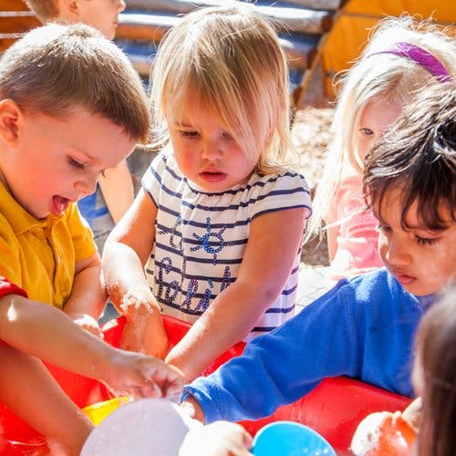 Children playing with water and toys in a red bin