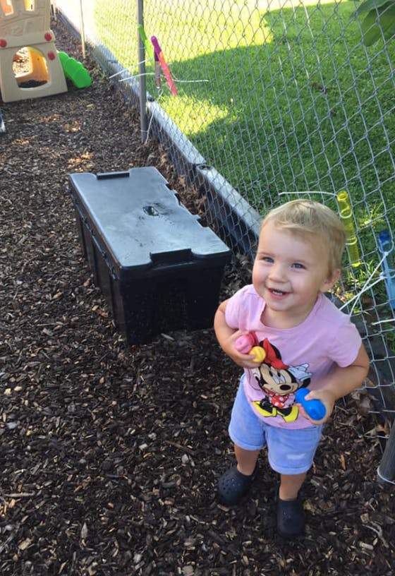 Child standing on wood chips holding toys