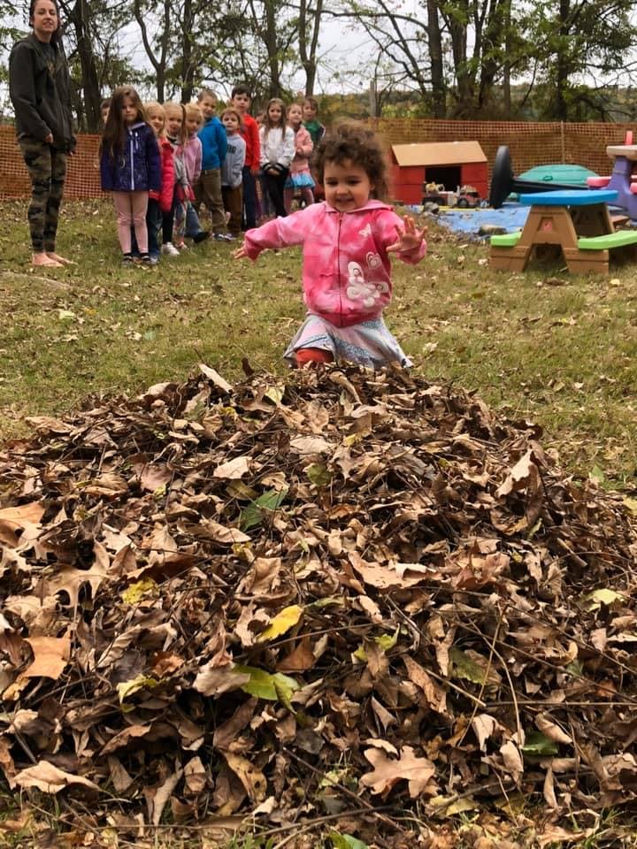 Child in pink jacket standing in a pile of leaves with other children in background