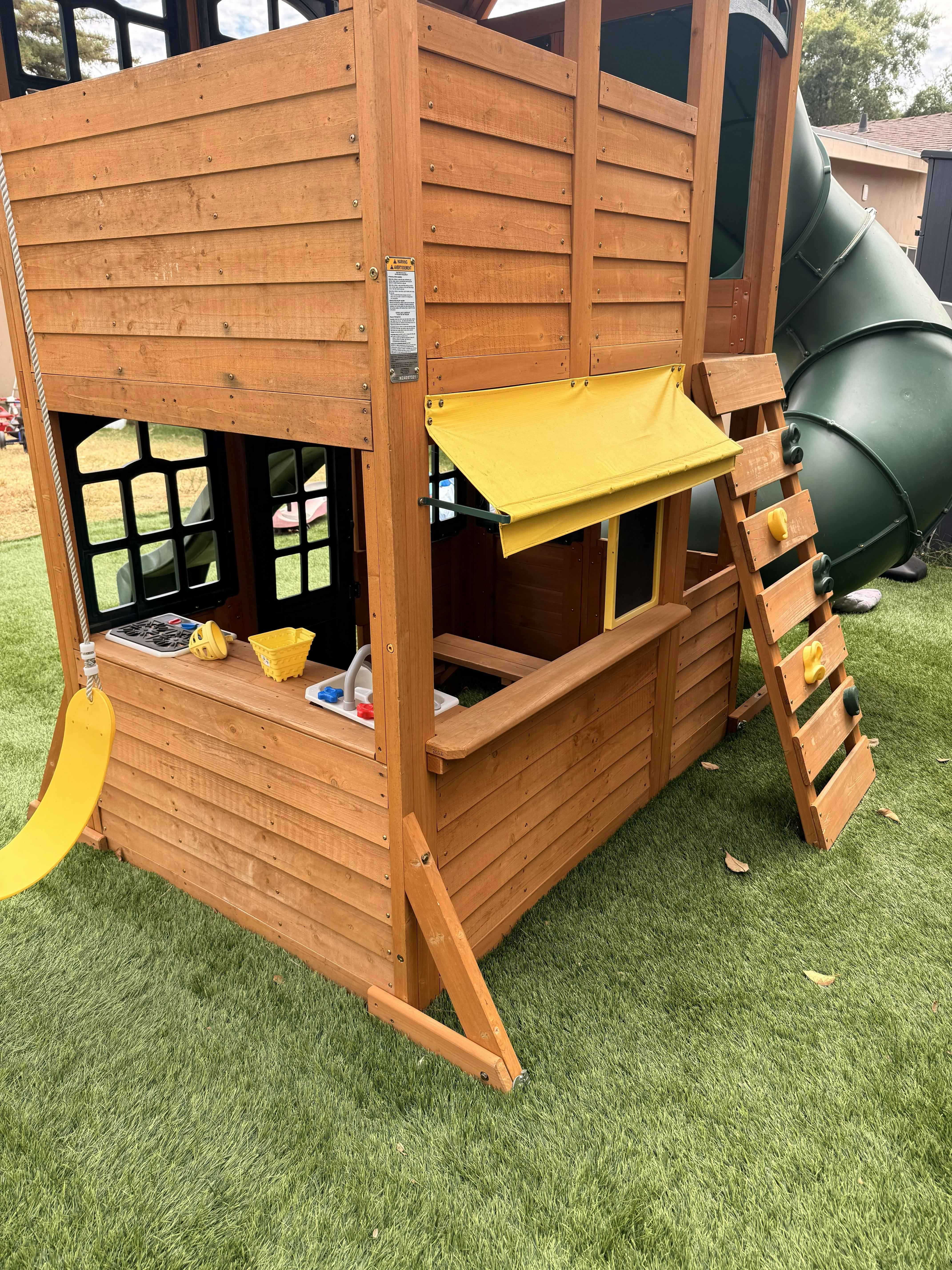Wooden outdoor playhouse with a slide and a play kitchen on artificial grass